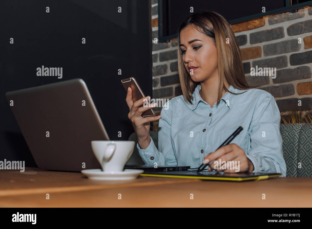 Female graphic designer working with laptop and using smartphone. - Image Stock Photo