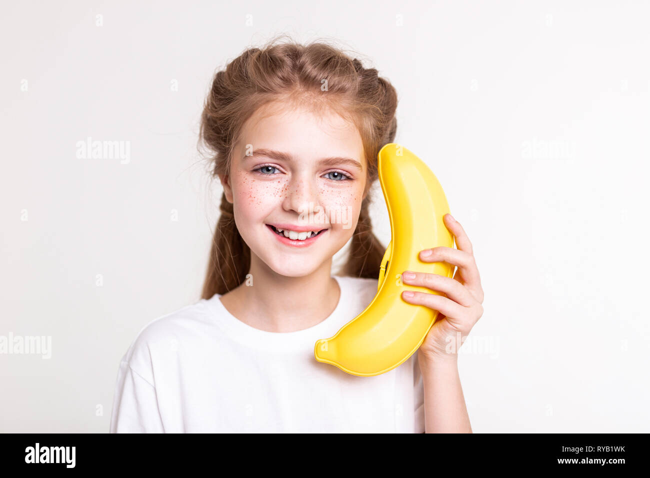 Smiling good-looking little lady keeping big orange fake banana Stock Photo