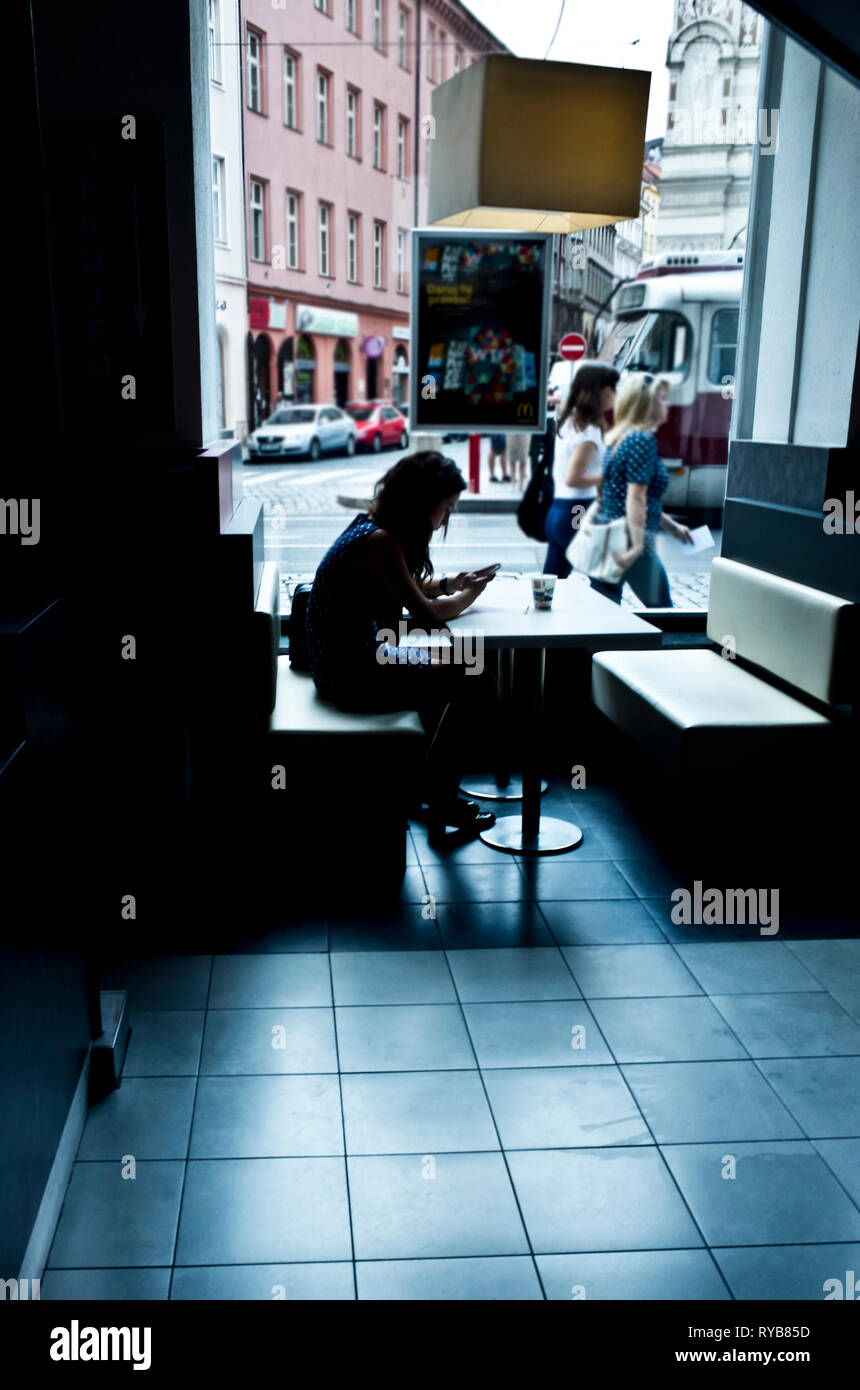 young woman sitting alone in a McDonal's restaurant in Prague Stock Photo