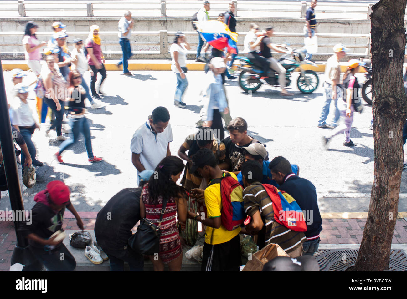 Demonstrators walk by while a group of homeless persons try to find some food in the garbage during a march  to protest against Nicolás Maduro. Stock Photo