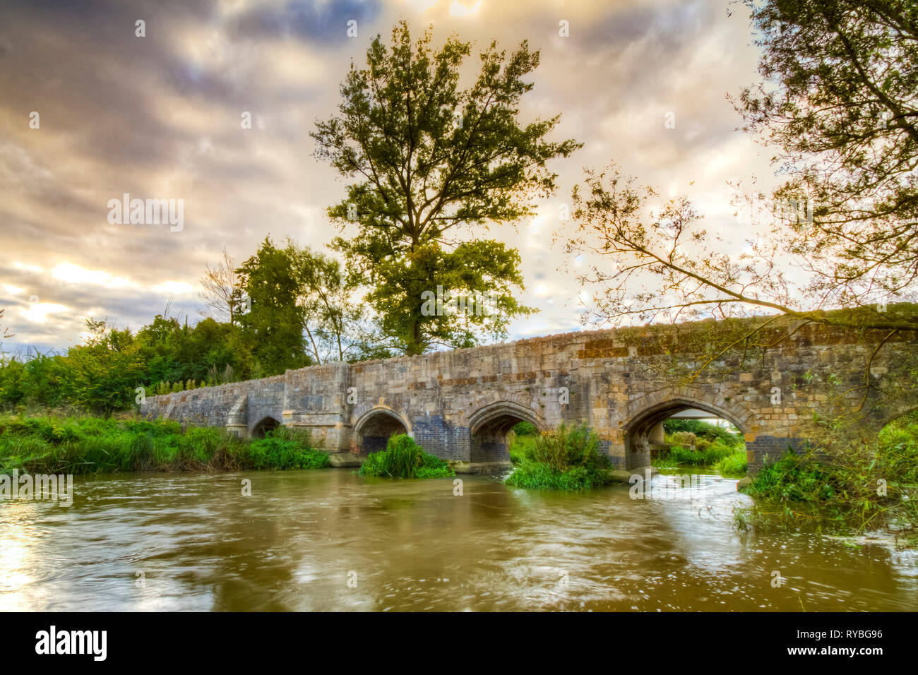 Old stone medival bridge over a streaming river in England. Dramatic cloudscape and old color tones Stock Photo