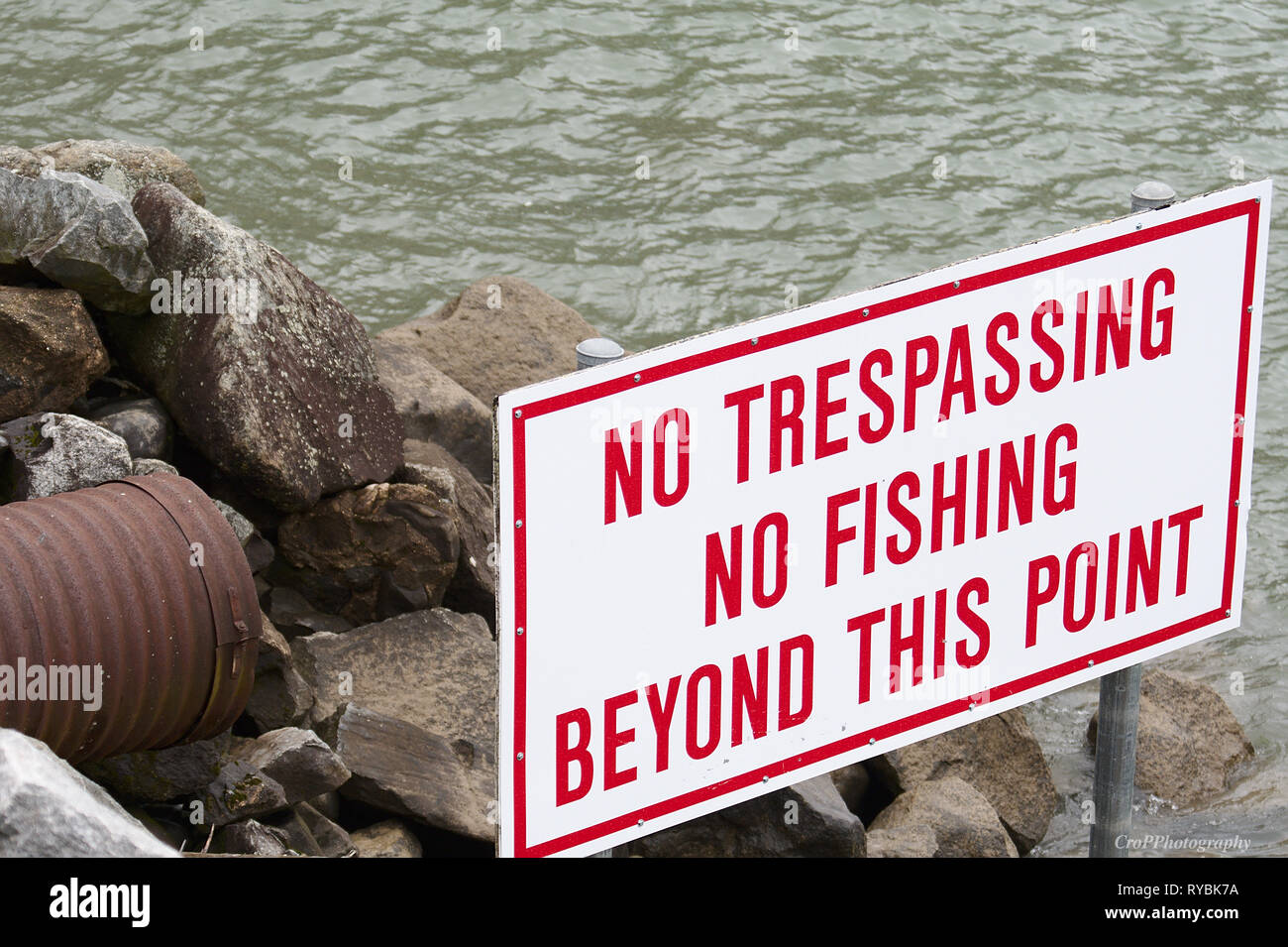 No trespassing and fishing sign near large drainage pipe Stock Photo