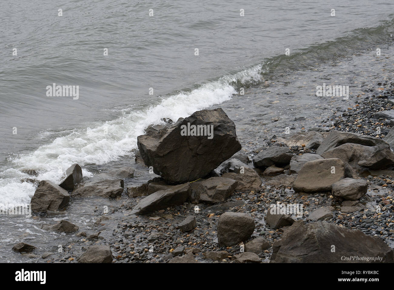 Incoming wave on shoreline with large boulder Stock Photo