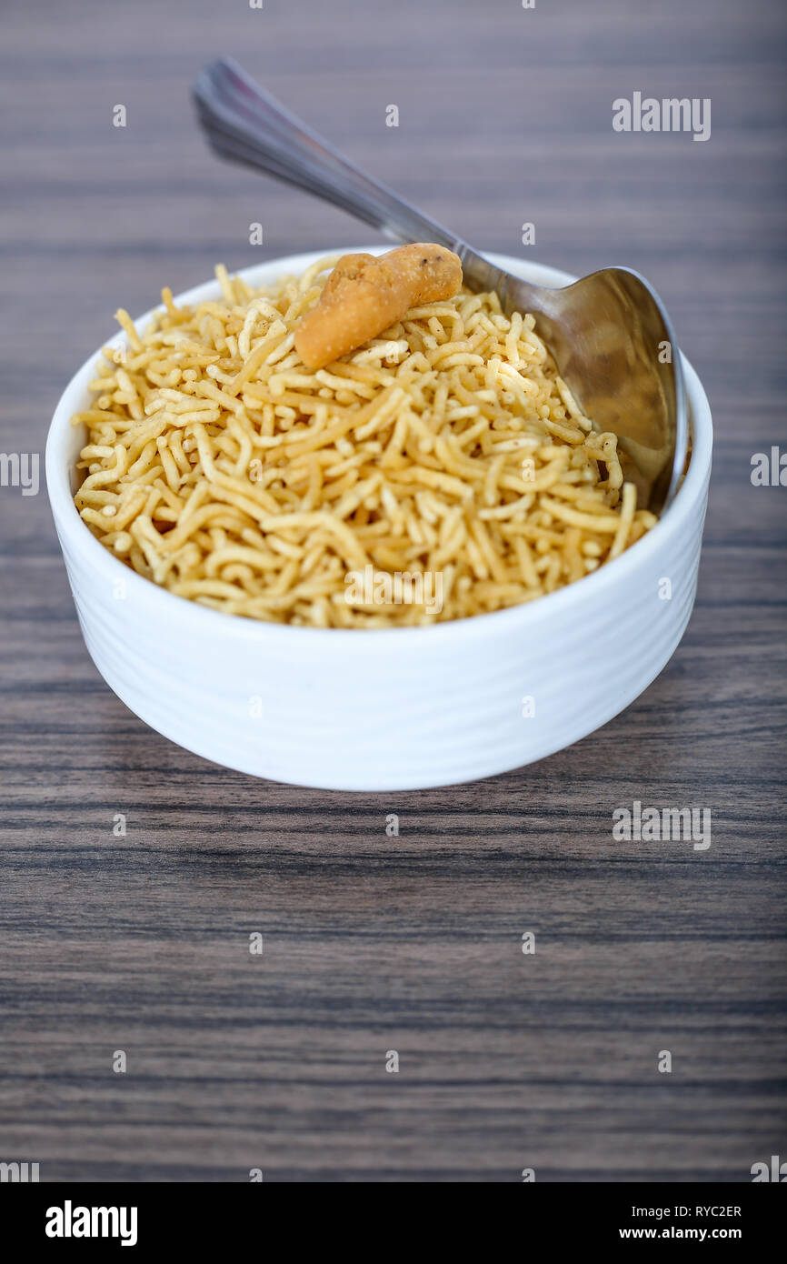 Namkeen bhujia in the bowl with spoon. Isolated on the wooden background. Stock Photo