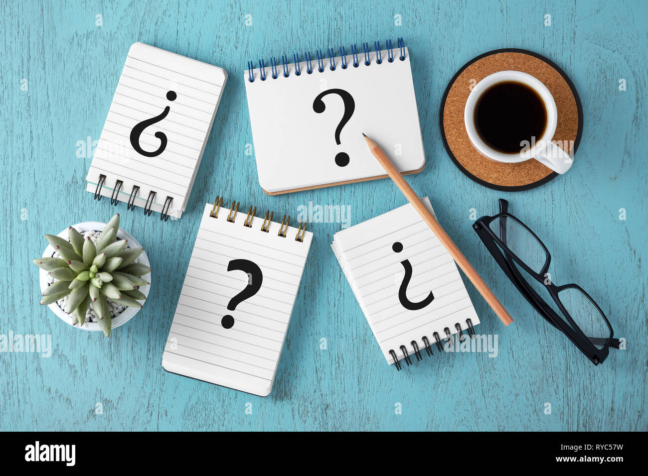 Question marks on notepads on blue wooden desk, variety of questions