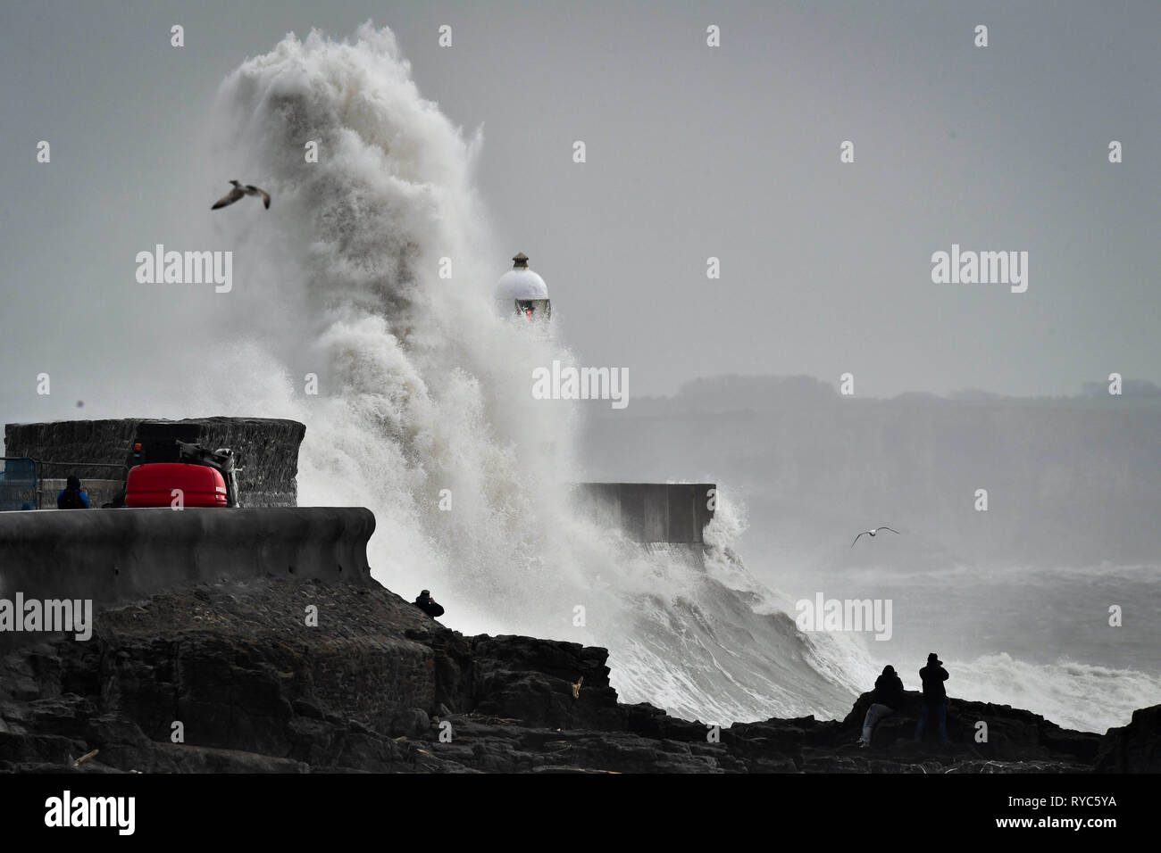Huge waves slap against the harbour wall as spectators watch from rocks