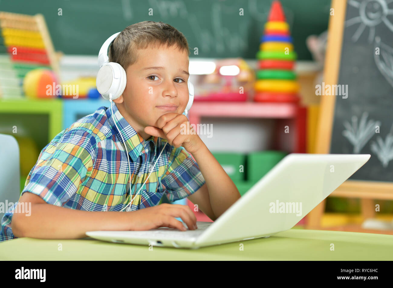 Portrait of little boy with headphones using laptop in classroom Stock ...