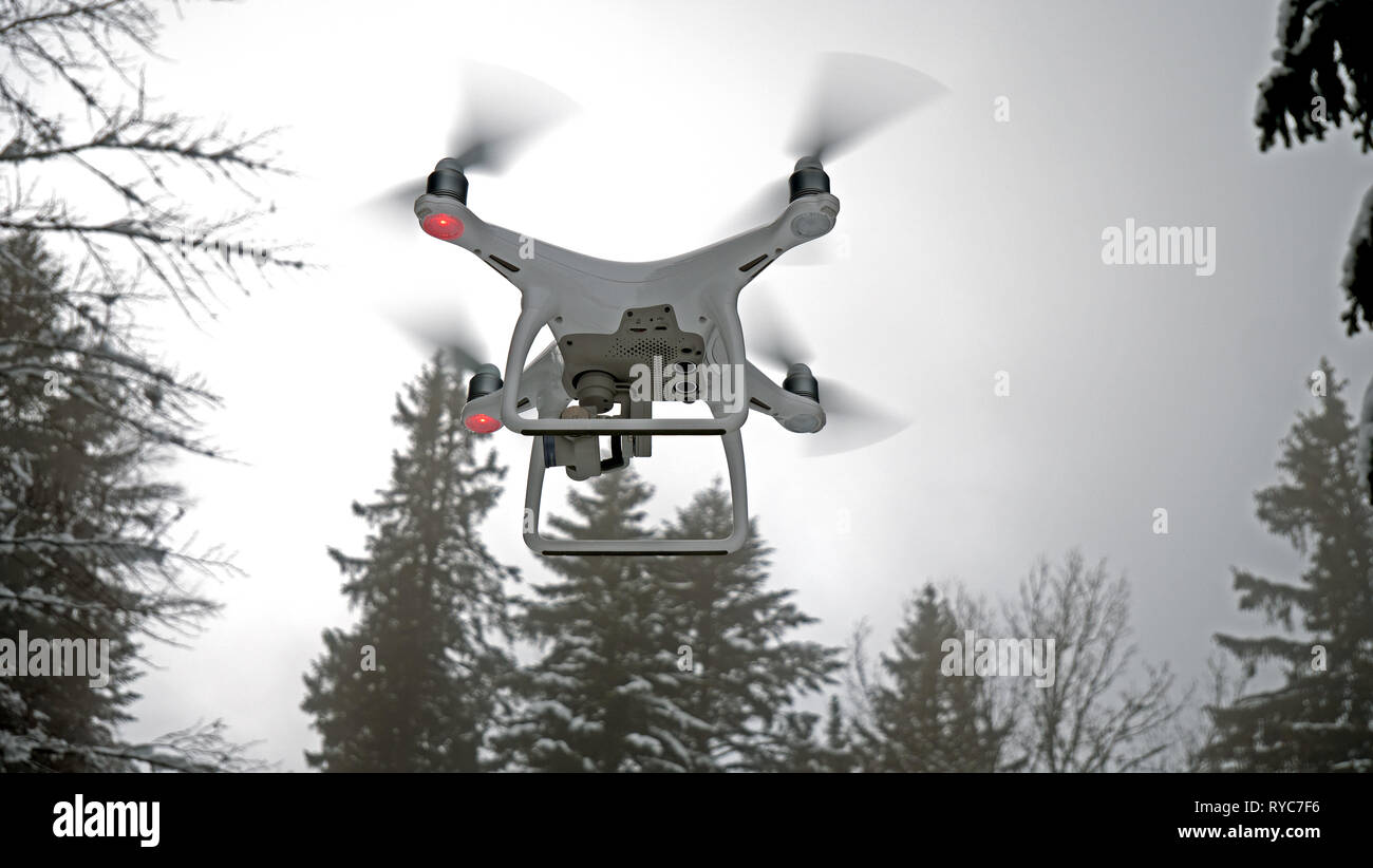 Close up photo of a hovering drone. The Aerial UAV is pictured in a winter, snowy environment in front of some snow covered alpine trees. Stock Photo