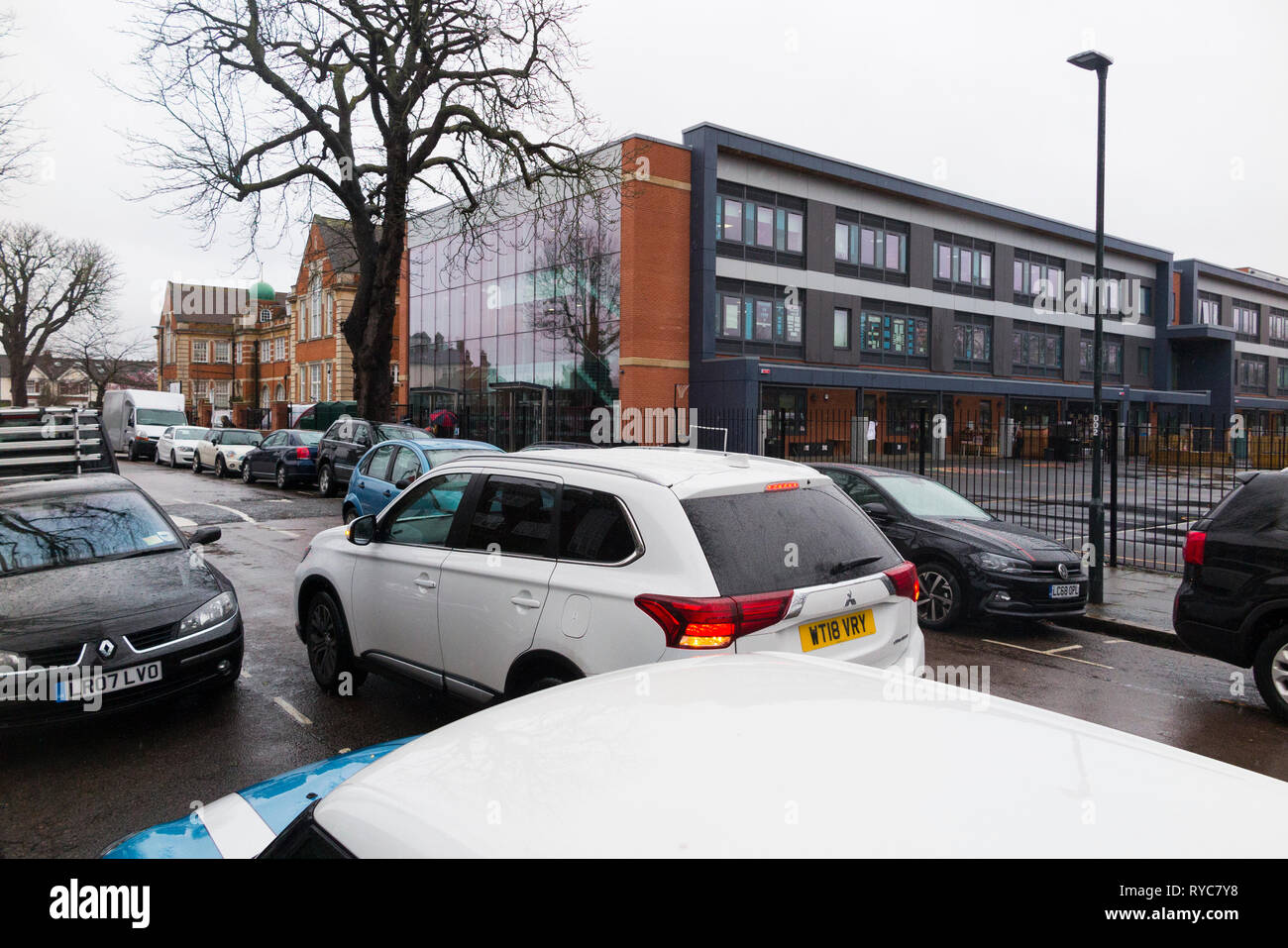 Cars parked dangerously / badly / illegally / double parking / double parked with hazard lights flashing during the school run drop off / collection UK Stock Photo