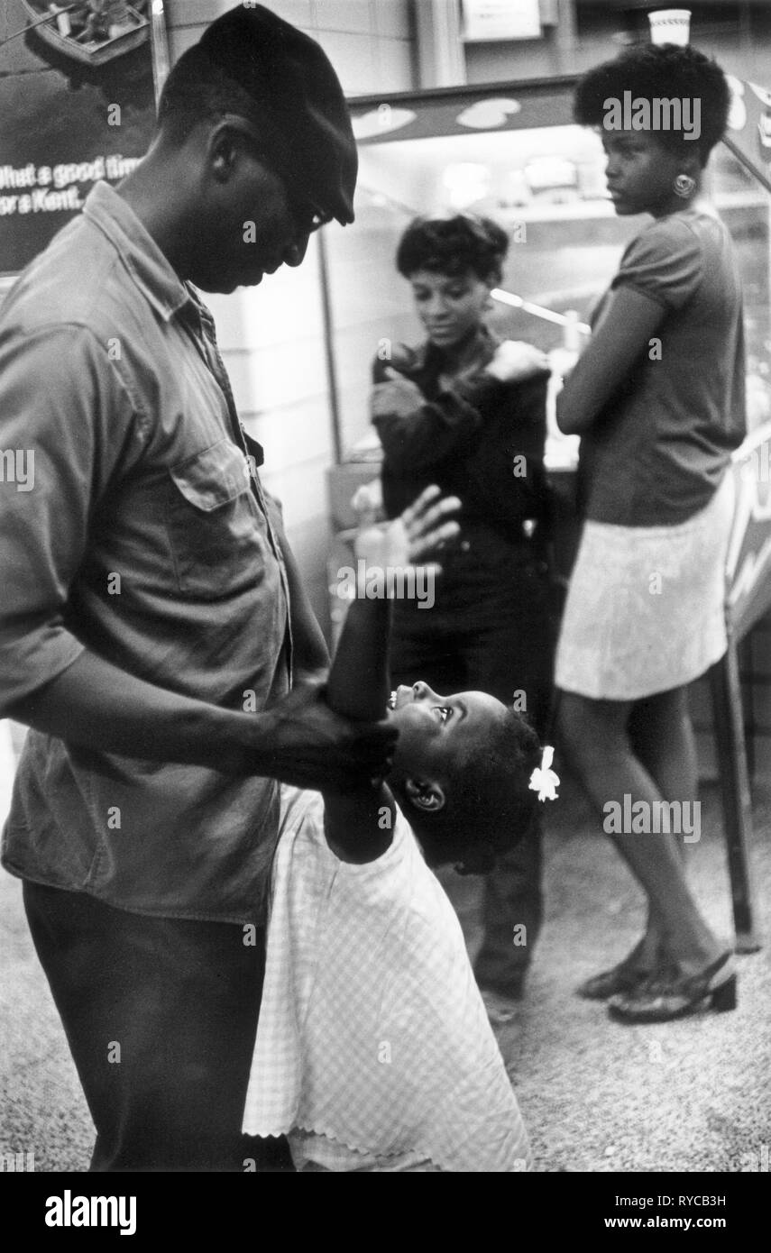 African American family group 1960s US. Father and daughter children play together while elder sisters lean against a Pin Ball machine. Late at night in a Greyhound bus station Washington DC US 60s. HOMER SYKES Stock Photo