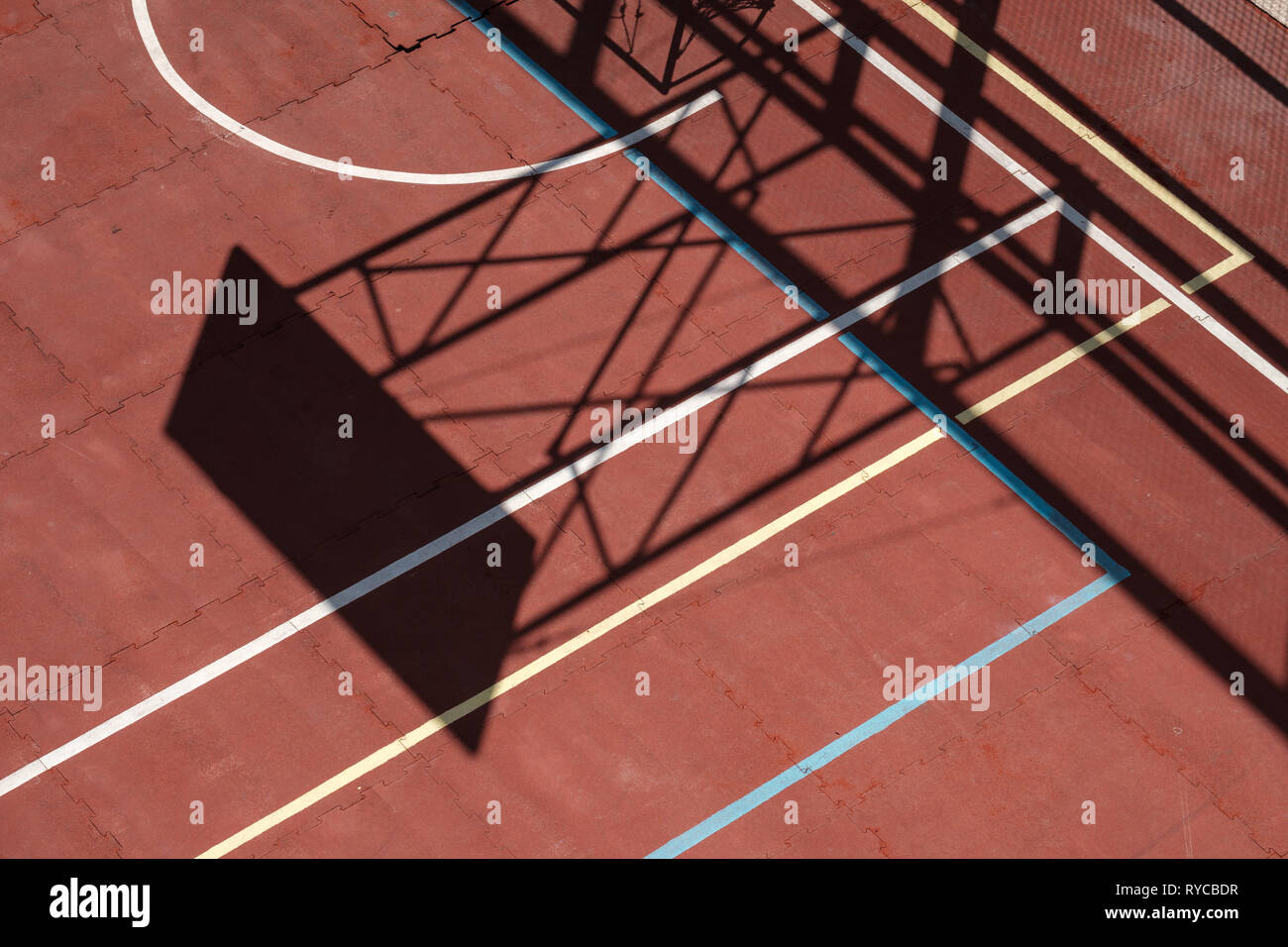 Semiabstract view of a red basketball court with sunlight and shadow