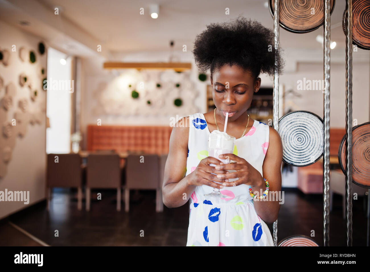 Сheerful african american young woman in summer dress at cafe drinking milkshake. Stock Photo