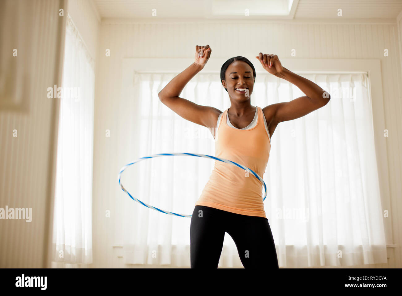 Happy young woman hula hooping in her living room. Stock Photo