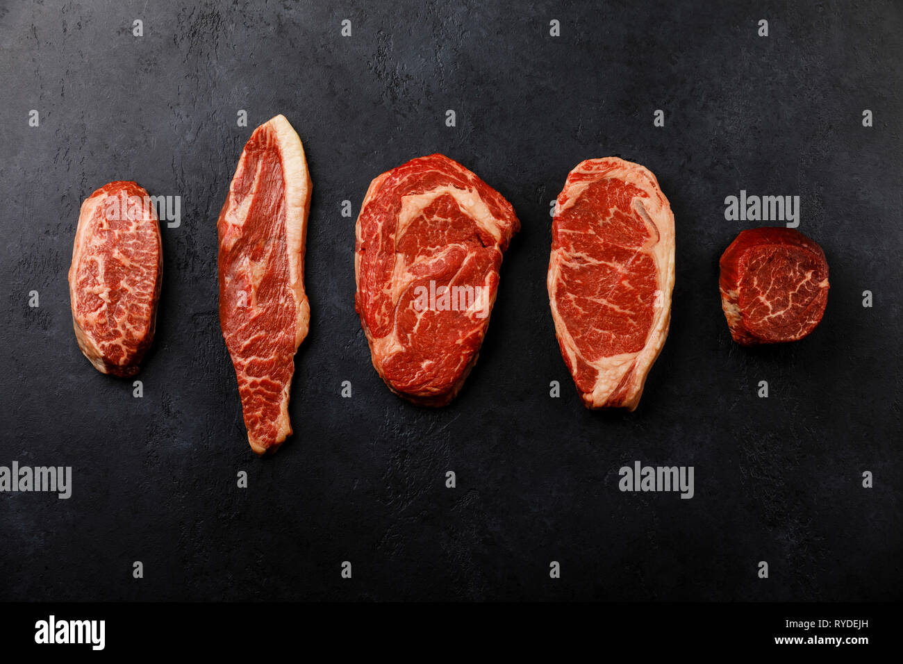Variety of Raw Black Angus Prime meat steaks Top Blade,  Top sirloin cap, Rib Eye, Striploin, Tenderloin fillet Mignon on dark background Stock Photo