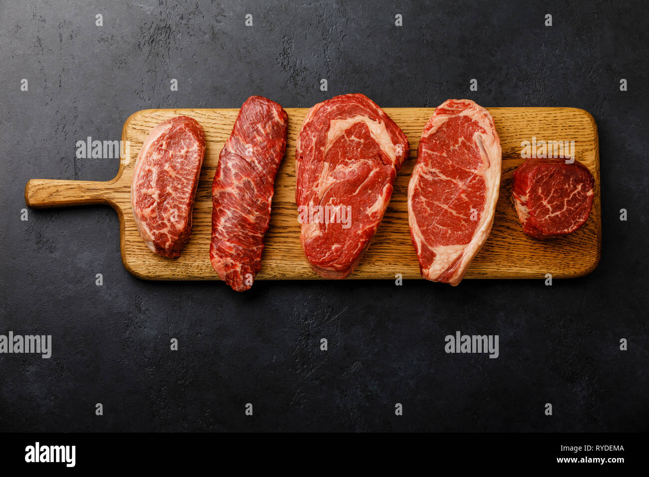 Variety of Raw Black Angus Prime meat steaks Top Blade, Denver, Rib Eye, Striploin, Tenderloin fillet Mignon on wooden board on dark background Stock Photo