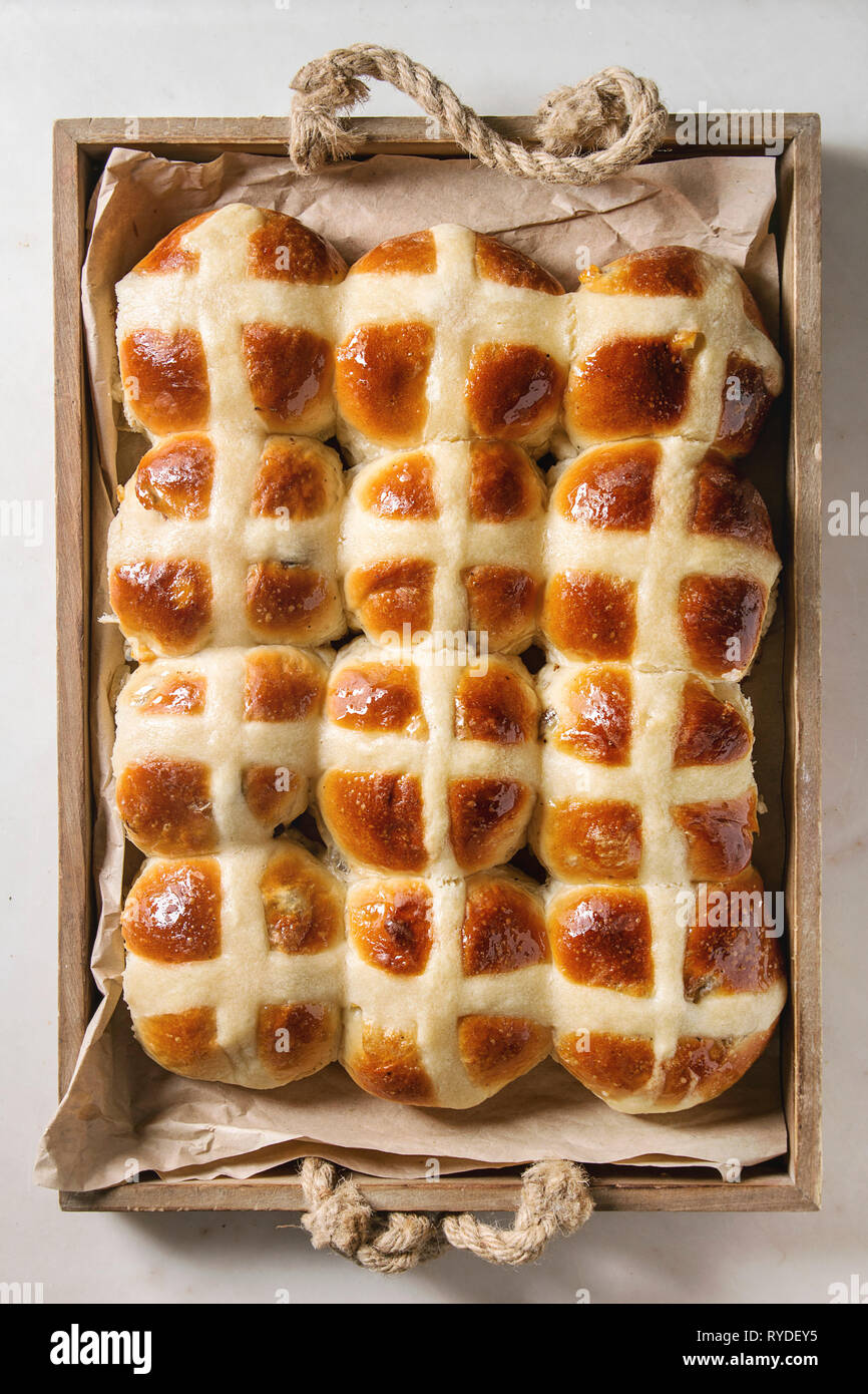 Homemade Easter traditional hot cross buns in wooden tray tray with baking paper over white marble background. Top view, space Stock Photo