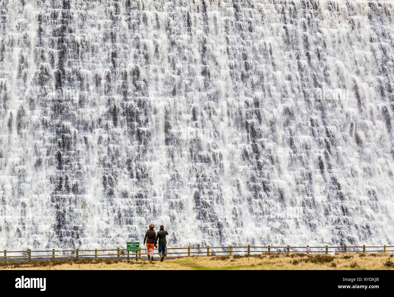 A couple watch water overflowing the Derwent Reservoir dam wall in the Derbyshire Peak District after weeks of heavy rain Stock Photo