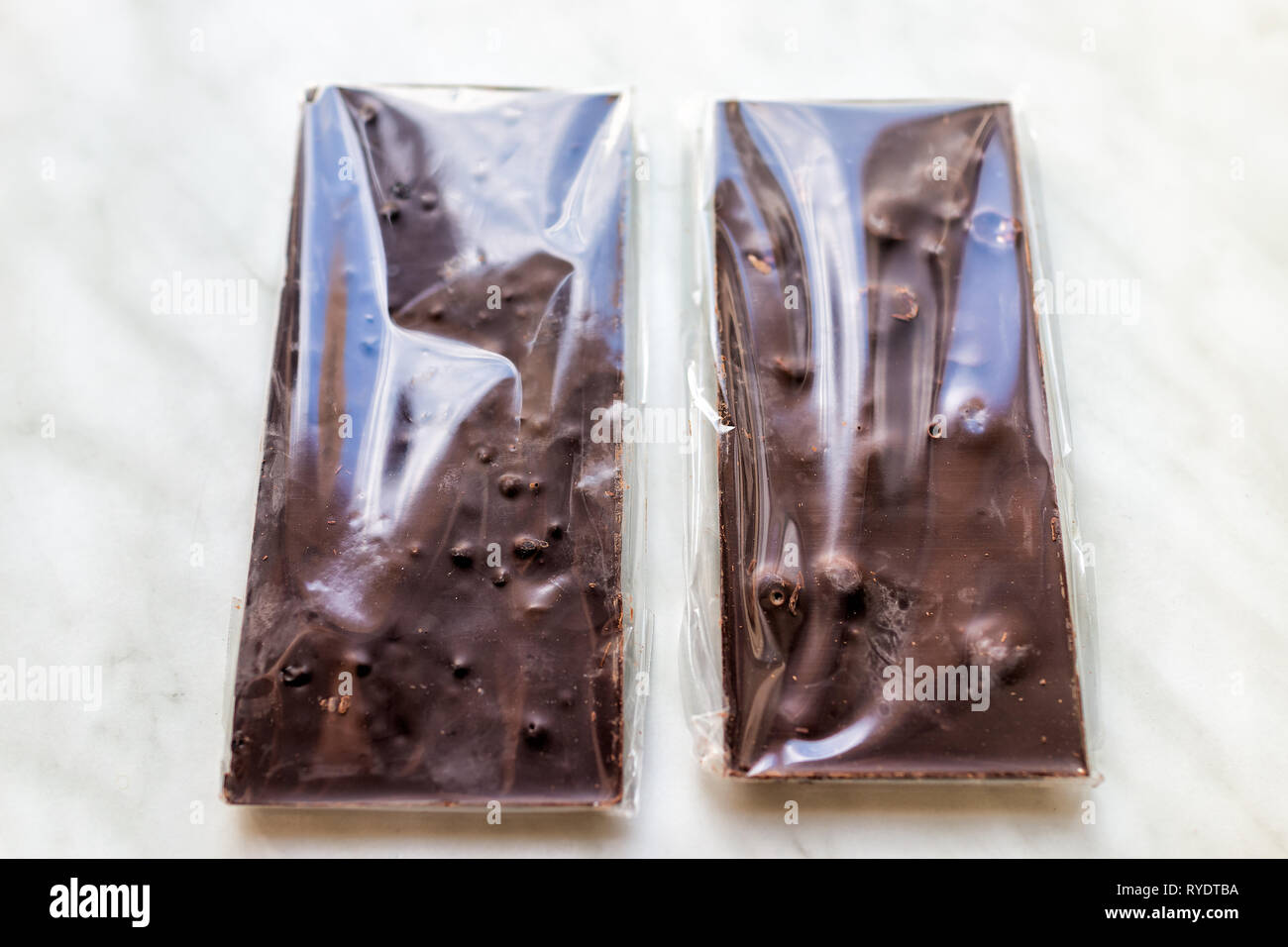 Flat top closeup of two packaged in plastic milk or dark chocolate bars with fruits and nuts hazelnuts almonds on table Stock Photo