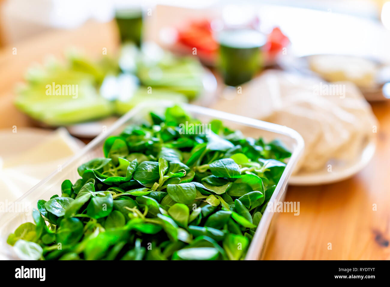 Wooden table setting of healthy vegan vegetarian lunch with macro closeup of packaged plastic box of lambs lettuce green vegetables with bokeh backgro Stock Photo