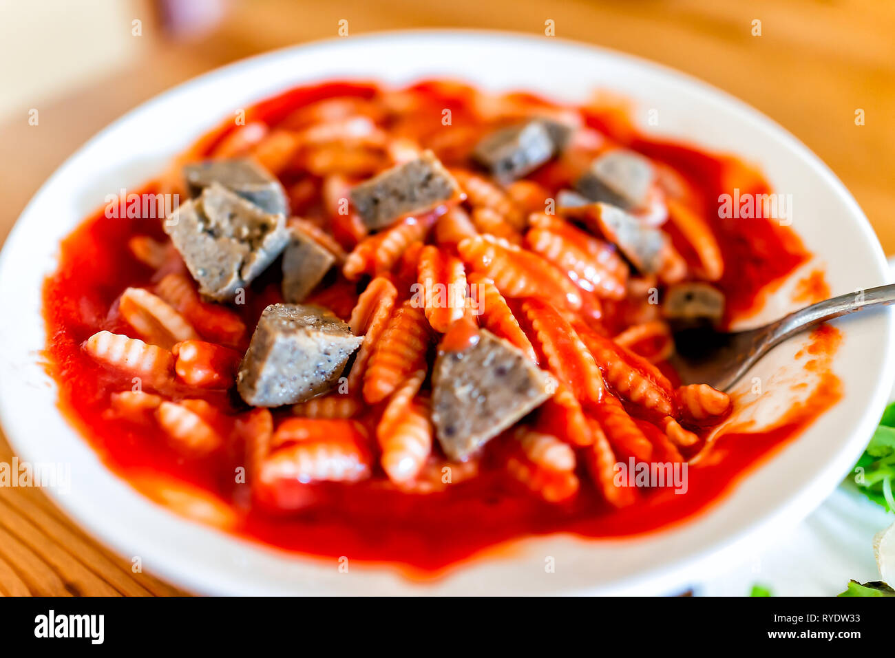 Closeup of bowl with sausage pieces and pasta gnocchi sardi Sardinian shape with red tomato marinara sauce with fork or spoon Stock Photo