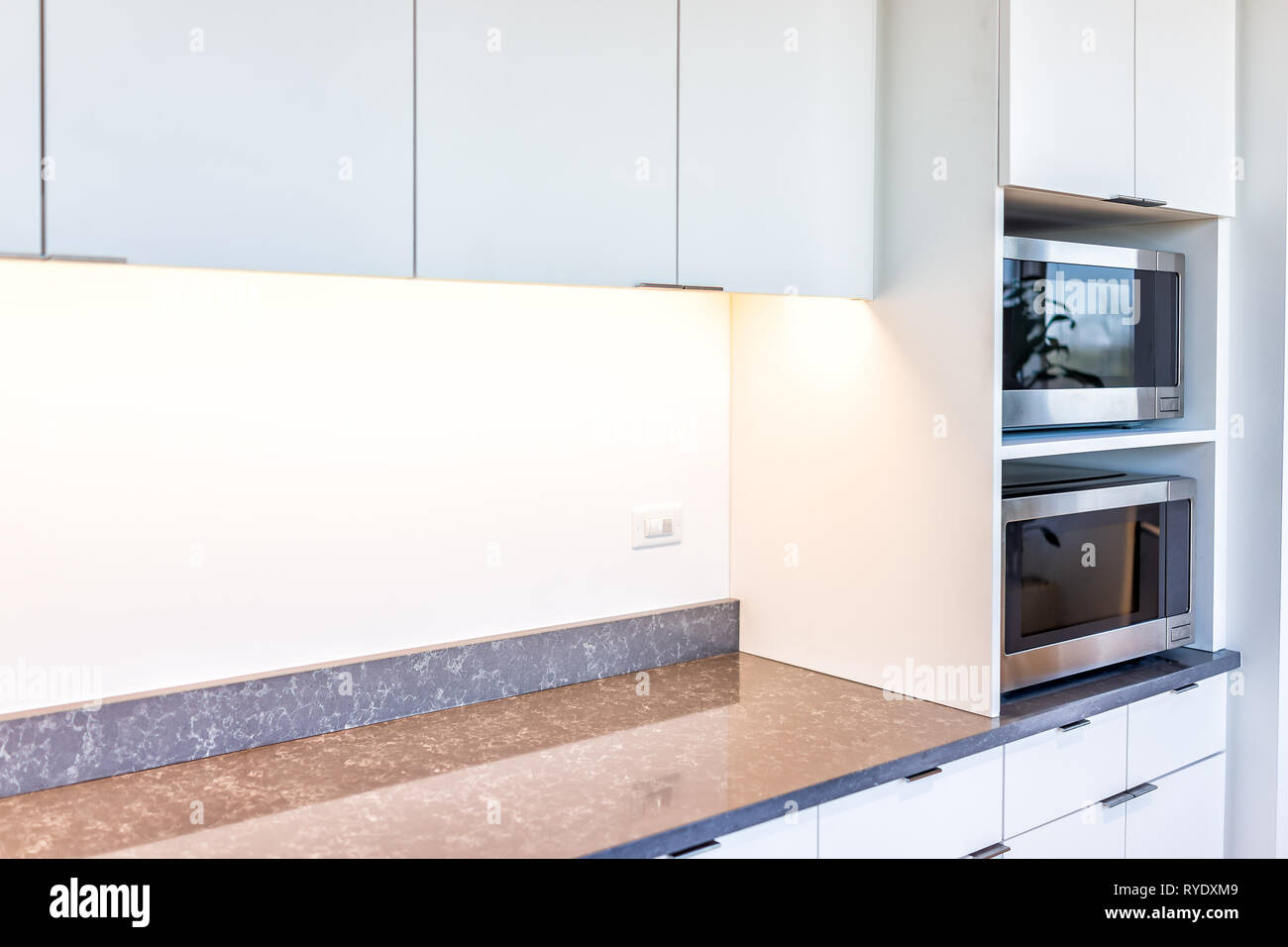 Modern white minimalist kitchen features cabinets with granite countertop and microwave toaster with empty space in office or home Stock Photo