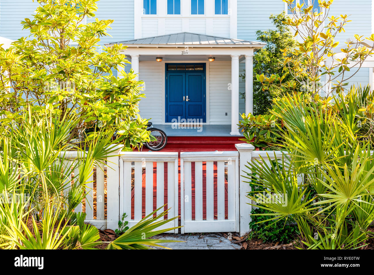 Seaside, USA - April 25, 2018: White and blue beach wooden wood architecture of house and door gate to front porch yard with green landscaping plants  Stock Photo