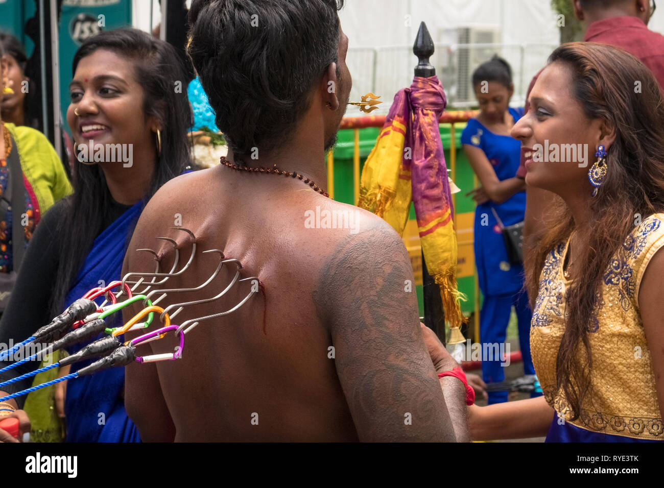 Large hooks pierced into devotee's back, with smiling girls - Thaipusam festival - Singapore Stock Photo