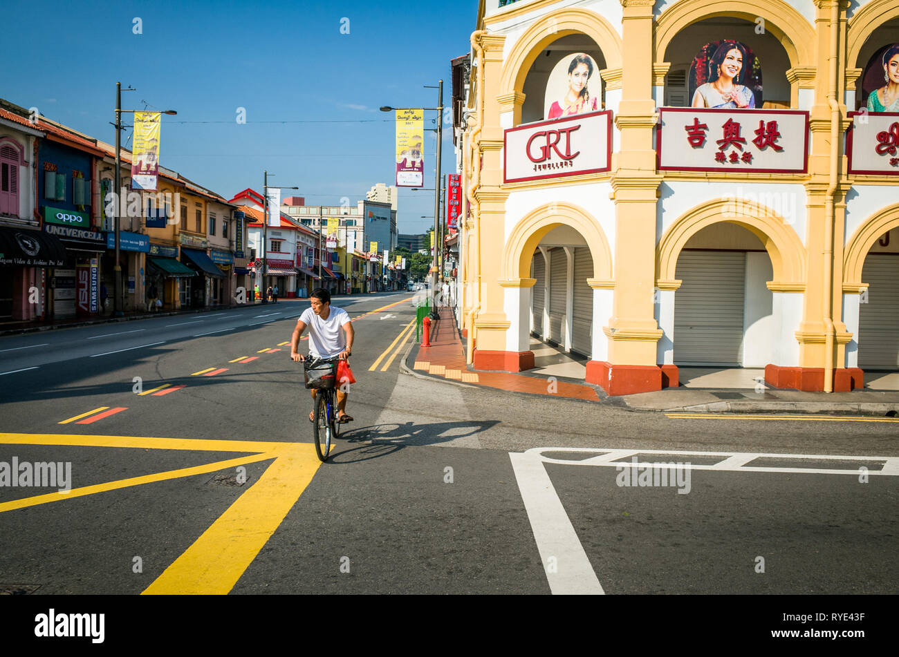 A Chinese man rides his bike across the crosswalk on empty Serangoon Road, Little India - Singapore Stock Photo