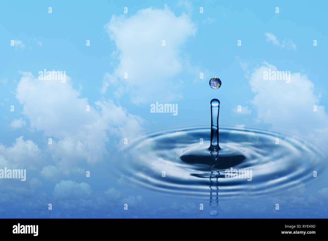 Drop of rain with earth image falling on smooth water surface. Blue sky and white clouds in background. Stock Photo