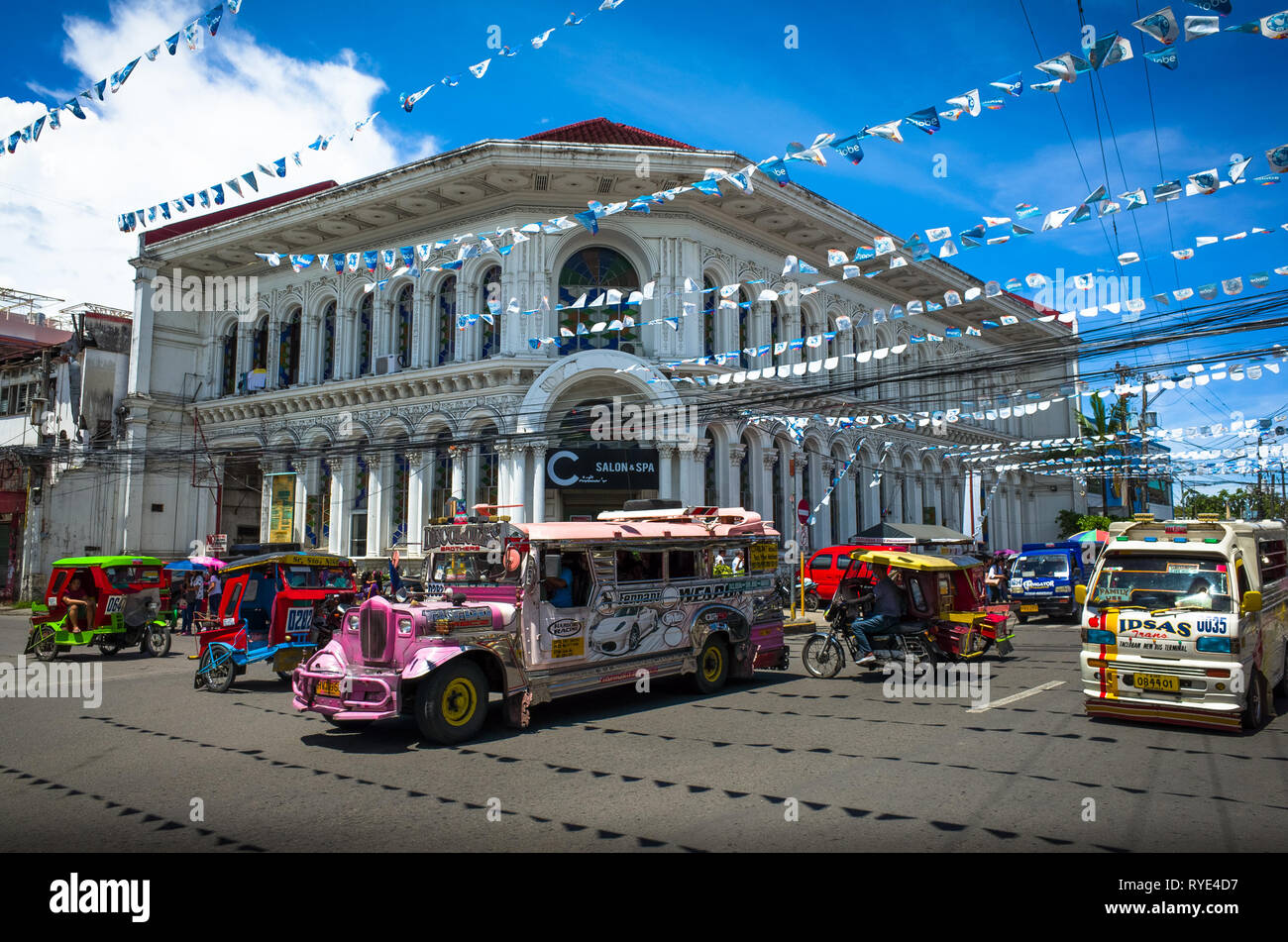 Pink Jeepney and colorful tricycle cross traffic with historic building - Tacloban City, Leyte - Philippines Stock Photo