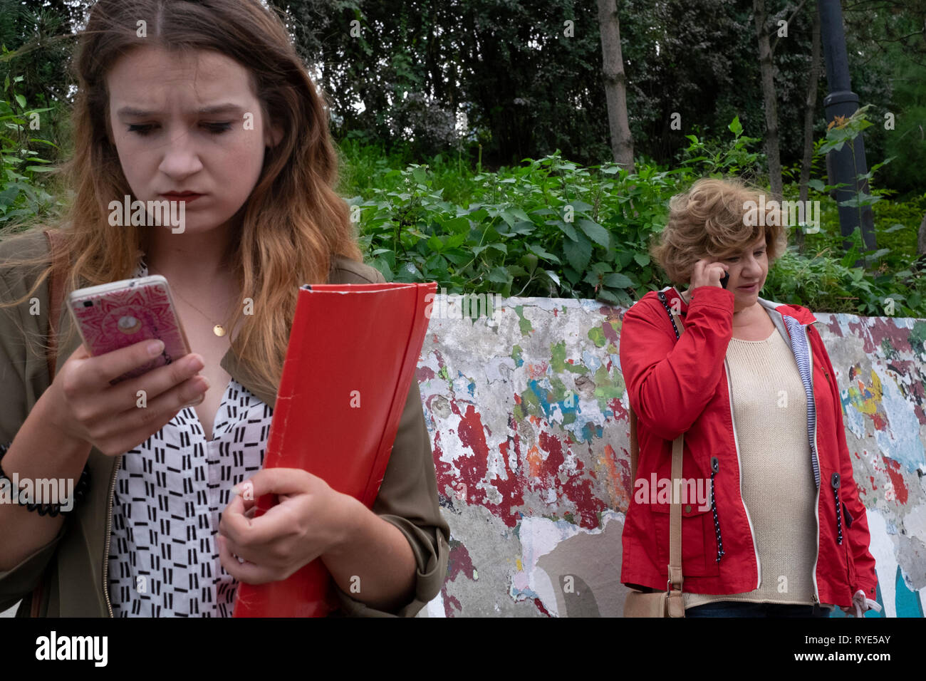 Two women engrossed in their cell phones by talking and texting in downtown Warsaw, Poland Stock Photo