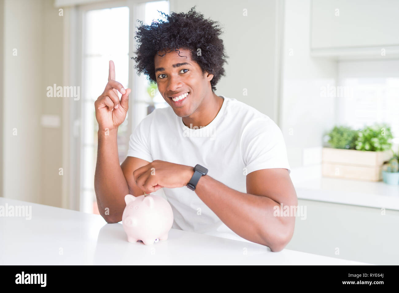 African American man putting a coin inside piggy bank surprised with an ...