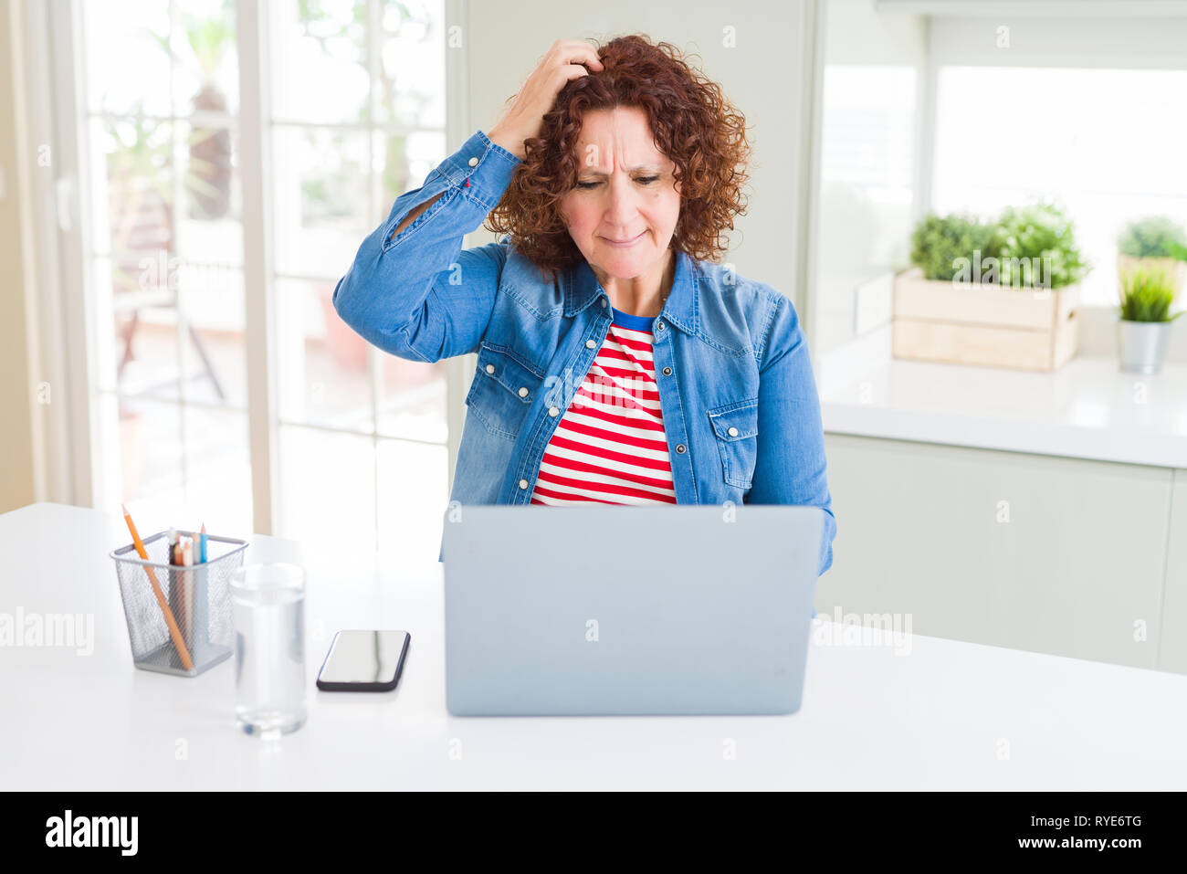 Senior woman working using computer laptop stressed with hand on head ...