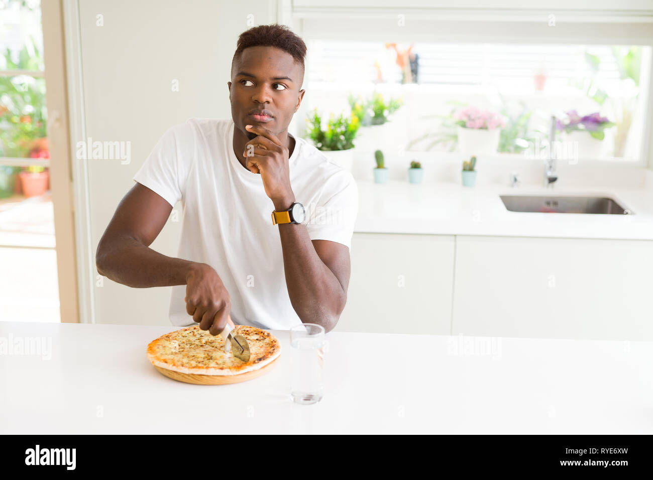African american man eating cheese pizza at home serious face thinking