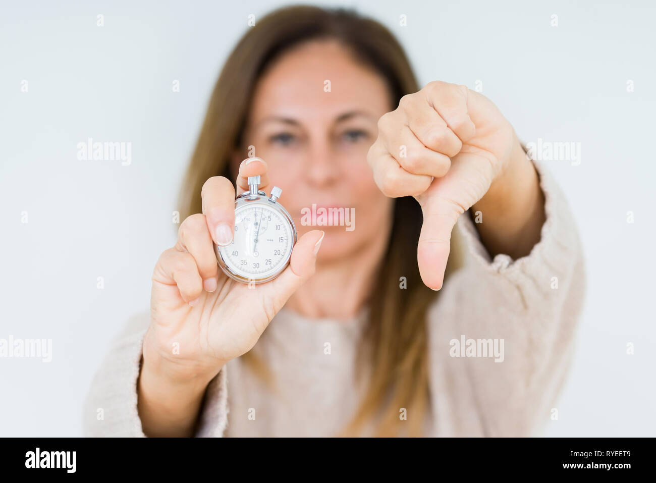 Middle age woman holding stopwatch isolated background with angry face ...