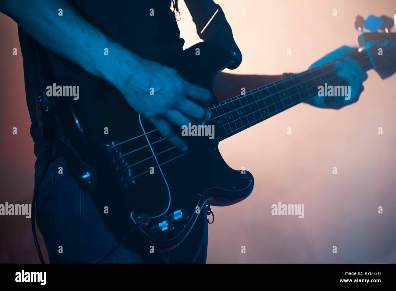 Live rock music background, electric bass guitar player in blue stage lights, closeup photo with soft selective focus Stock Photo