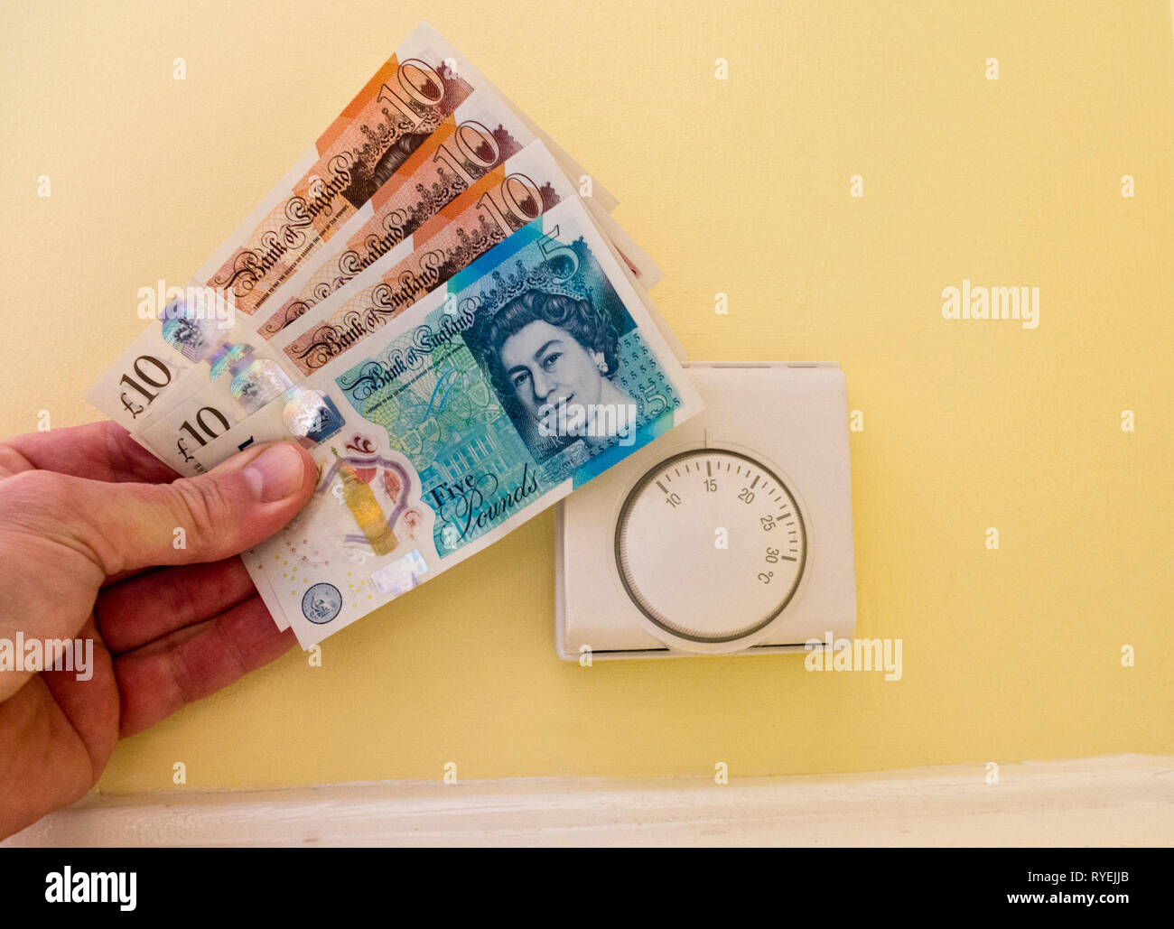Honeywell Central Heating Room Thermostat With Man's Hand Holding Pound Sterling Notes Money Regarding Heating Costs, UK Stock Photo