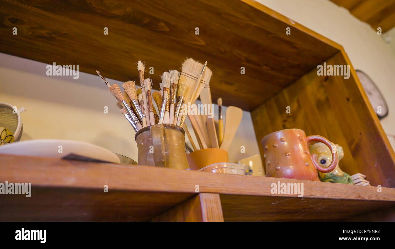 Sort Of Paint Brushes Inside The Mug On The Shelf With Other