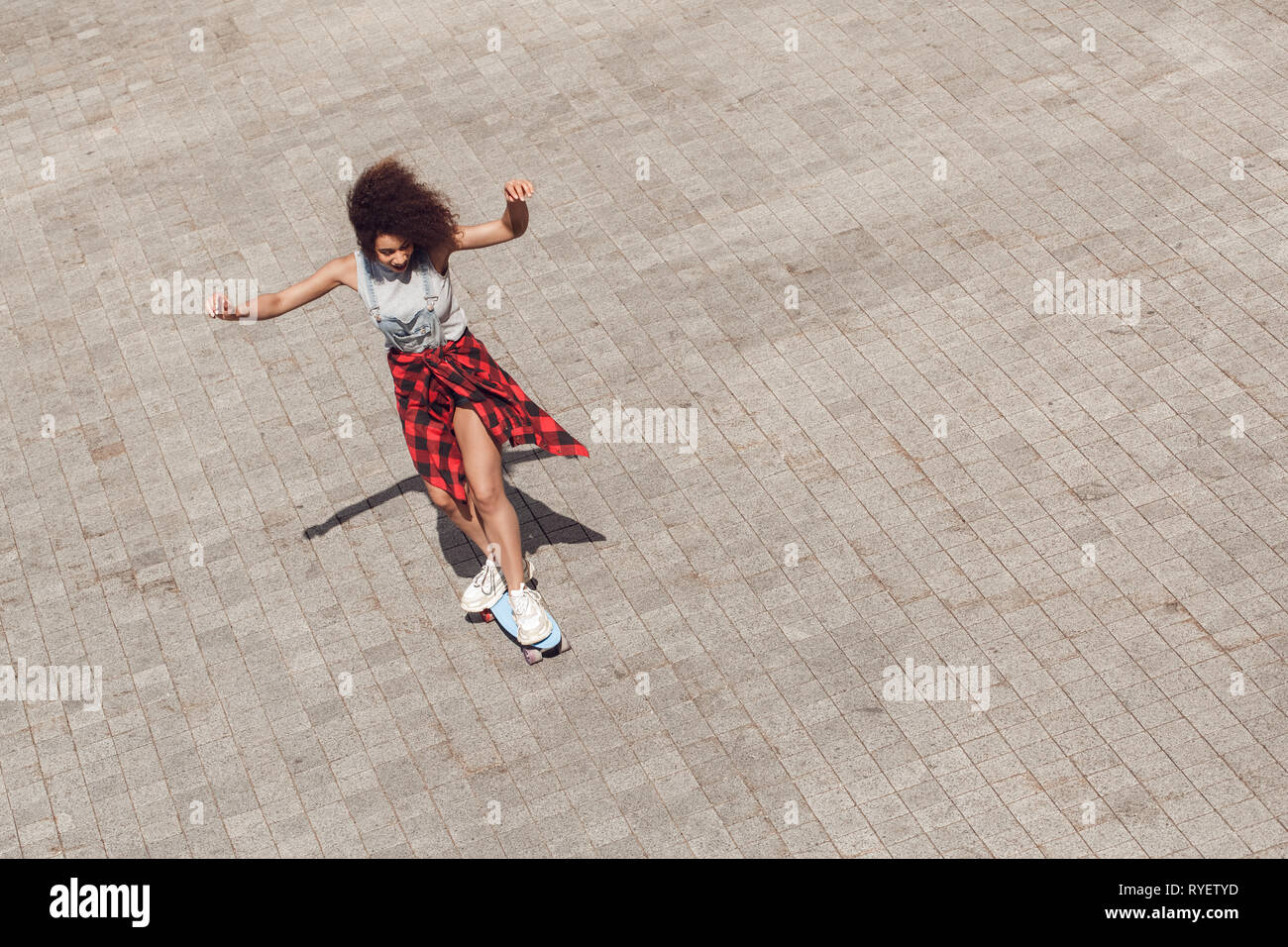 Young woman in the city street riding penny board hands up cheerful top ...