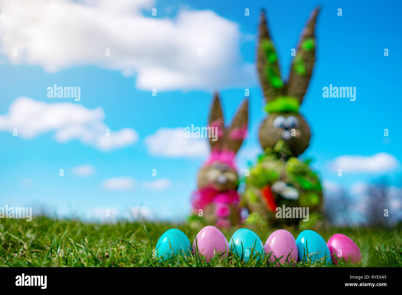 Straw Figure Bunny With Colorful Easter Eggs green grassand blue sky Easter And Spring Background. blur Stock Photo