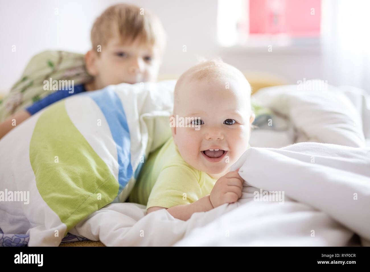 Siblings playing on bed at home. Baby girl and older brother having fun together. Stock Photo