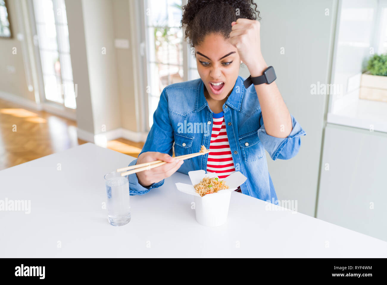 Young african american woman eating asian noodles from delivery box annoyed and frustrated shouting with anger, crazy and yelling with raised hand, an Stock Photo