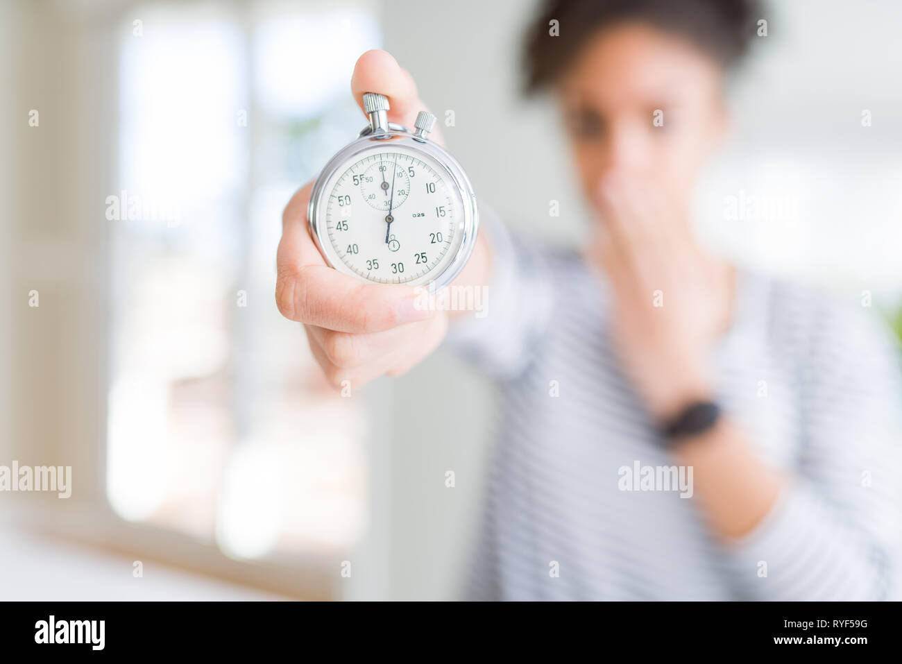 Young african american woman holding stopwatch cover mouth with hand ...