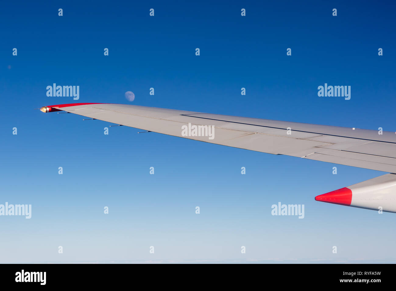 Aircraft wing with moon and blue sky taken from aircraft window Stock Photo