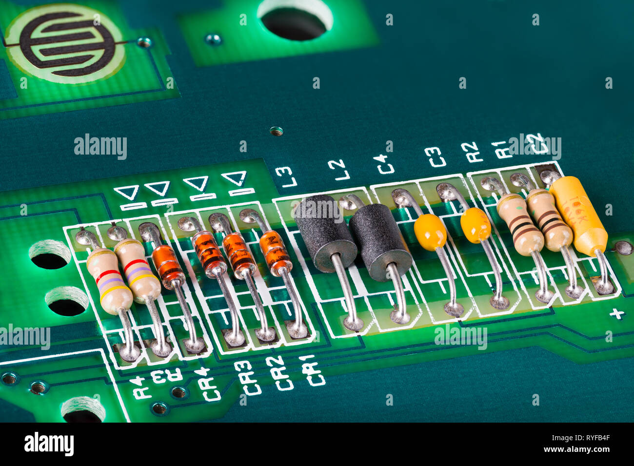 Inductors, capacitors, resistors and diodes on PCB. Colorful electronic components detail. Green circuit board. Button switch. Open computer keyboard. Stock Photo