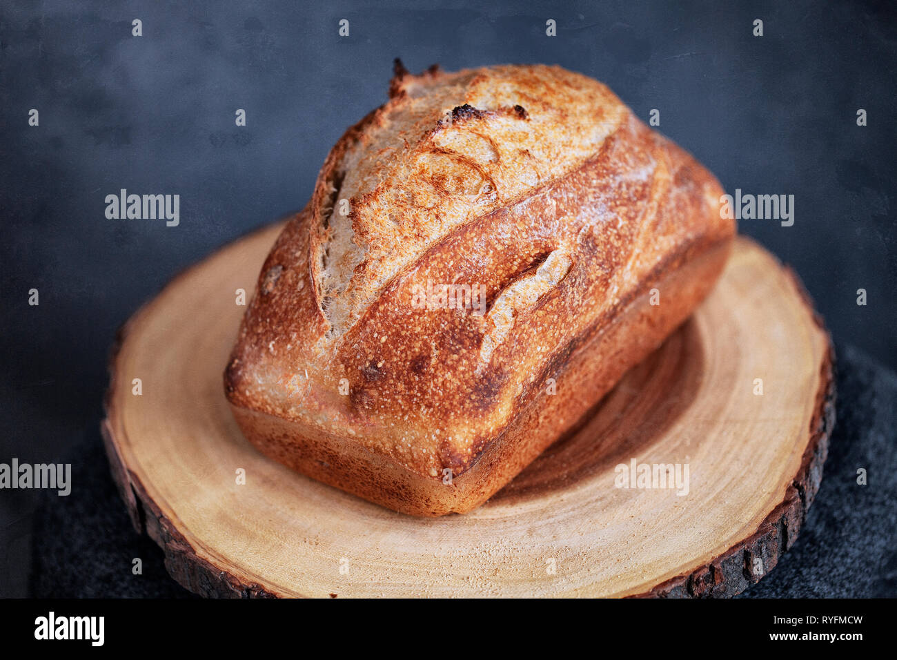 rectangle loaf of freshly baked homemade artisan sourdough bread on a round wood plank - image Stock Photo