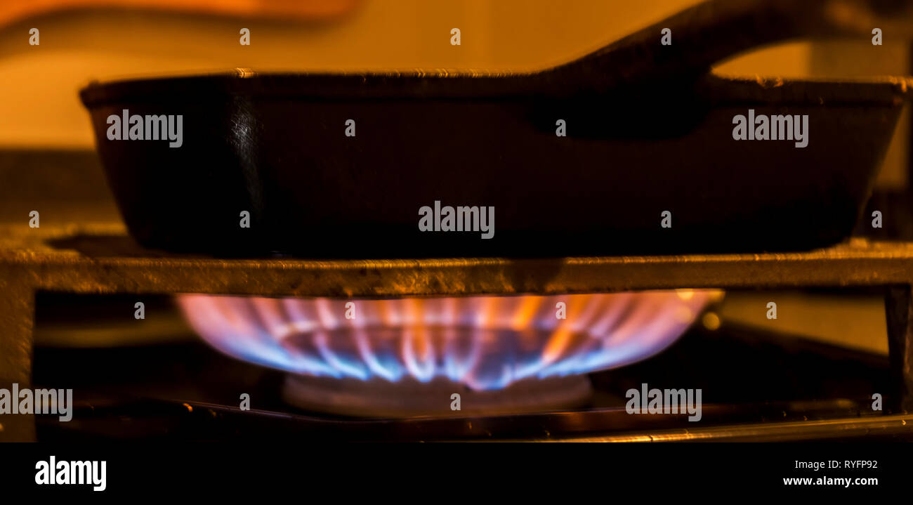 A flame from a gas stove burns under a black cast iron frying pan Stock