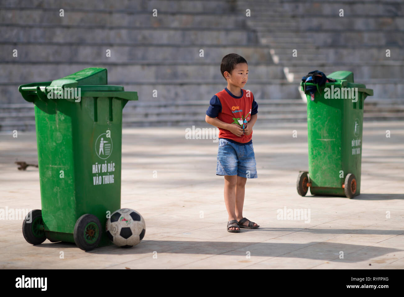 A vietnamese kid playing soccer as goalkeeper with a goal made with two green garbage bins in Sa Pa, Lao Cai, Vietnam Stock Photo