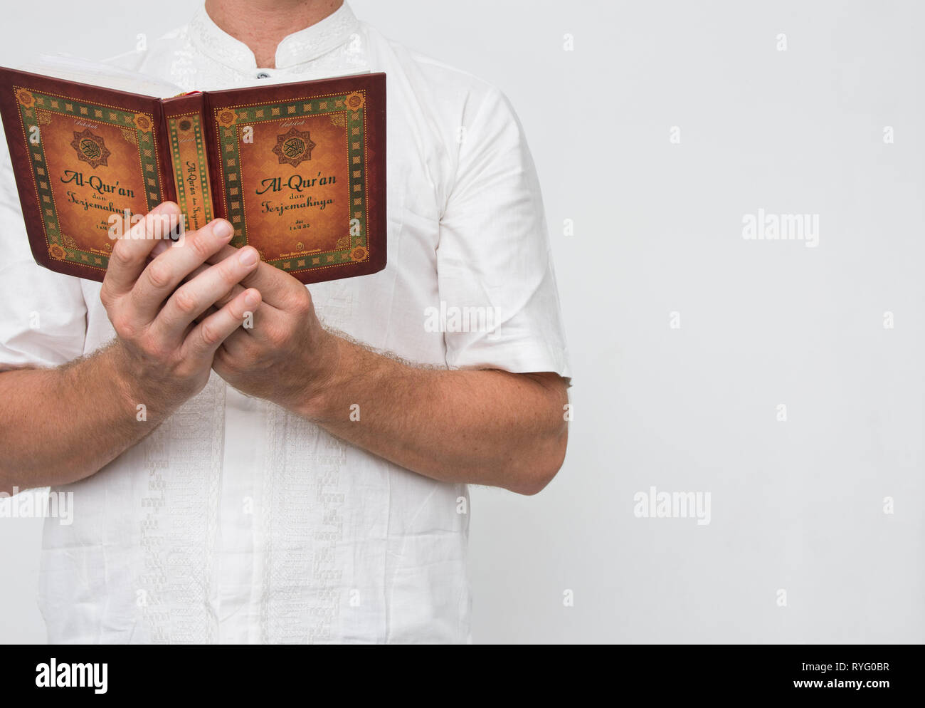 Man wearing white standing reading Al-Quran with copy space. Stock Photo
