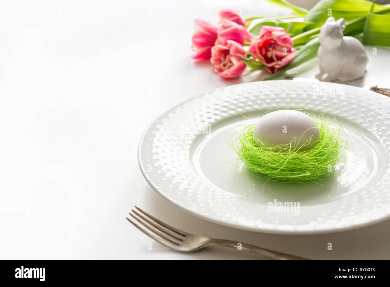 Easter table setting with pink tulip on white. Spring romantic dinner. Space for your text. Stock Photo